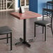 A Lancaster Table & Seating butcher block table with mahogany finish and cast iron base plate with two black chairs at a restaurant table.