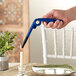A hand holding a blue Scripto multi-purpose lighter over a table with a lit candle in a glass holder.