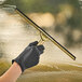 A hand wearing a black glove using an Ettore Master brass squeegee to clean a window.