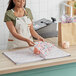 A woman in an apron holding a pack of SatinWrap Liberty Bloom tissue paper sheets.