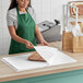 A woman in a green apron cutting SatinWrap tissue paper on a wooden cutting board.