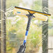 A hand in a black glove using an Ettore blue and yellow squeegee to clean a window.