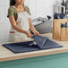 A woman in an apron using SatinWrap Midnight Blue tissue paper to wrap a bag on a counter.