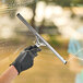 A hand in a black glove using an Ettore Master stainless steel squeegee to clean a window.