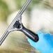 A hand in a blue glove holding an Ettore ProGrip window squeegee with a black handle.