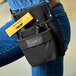 A woman wearing blue jeans and a tool belt with an Ettore multi-use utility pouch holding a yellow scraper.