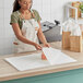 A woman in an apron using SatinWrap Gold Reflections tissue paper to wrap a doughnut.