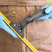 A person wearing blue gloves using an Ettore stainless steel window squeegee with a yellow foam grip.