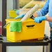 A person wearing blue gloves holding a yellow rectangular Ettore bucket.