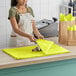 A woman using SatinWrap Limon tissue paper to wrap a yellow bag on a counter.