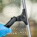 A hand in blue gloves using an Ettore Contour Pro+ squeegee to clean a window.