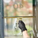 A hand wearing a black glove using an Ettore Master brass squeegee to clean a window.