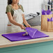 A woman in an apron using SatinWrap pansy tissue paper to wrap a purple cloth.