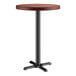 A Lancaster Table & Seating round wooden bar table with a mahogany finish and a black cast iron base.