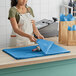 A woman in an apron using SatinWrap Fiesta Blue tissue paper to wrap a blue plate.