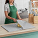 A woman in a green apron using SatinWrap silver tissue paper to wrap a paper bag on a counter.