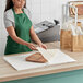 A woman wearing a green apron cutting a gold star tissue paper sheet on a wooden cutting board.