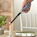 A hand holding a Scripto Aim 'N Flame Max Multi-Purpose Lighter over a candle in a glass holder.