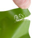 A hand holding a green Basic Earth Botanicals shower cap in a clear bag.