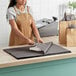 A woman in an apron using SatinWrap Slate Gray tissue paper to wrap a piece of paper.