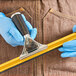 A person wearing blue gloves using a stainless steel squeegee handle with a black rubber grip to cut fabric.