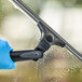 A hand in a blue glove using an Ettore Contour Pro+ squeegee to clean a window