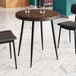 A Lancaster Table & Seating round butcher block table with black legs and two black chairs.