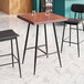 A Lancaster Table & Seating butcher block table with mahogany finish and black legs with two black bar stools.
