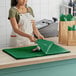 A woman in an apron using green SatinWrap tissue paper to wrap a bottle.