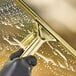 A hand wearing black gloves using an Ettore brass squeegee handle to clean a window.