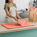 A woman wearing an apron putting a bag of coral tissue paper on a counter.