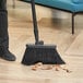 A person sweeping the floor with a Lavex black angled broom head.