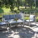 An Outdoor Interiors white aluminum sofa with blue cushions on a patio with a table and chairs.