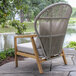 An Outdoor Interiors teak and white wicker parlor chair with a gray Sunbrella cushion on a stone patio.