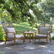 An Outdoor Interiors teak and white wicker parlor chair with a gray Sunbrella cushion on a stone patio.