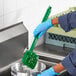 A person in blue gloves using a green Lavex floating pot scrub brush to clean a sink.