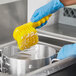 A person in blue gloves scrubbing a pot with a Lavex yellow brush.