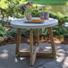 An Outdoor Interiors ivory and eucalyptus round accent table with a plate of food and a bowl of oranges on it.