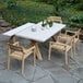 Outdoor Interiors Antique Wash Eucalyptus Stackable Dining Chairs on a table on an outdoor patio.