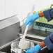 A person wearing blue gloves using a white Lavex pot scrub brush to stir food in a pot.