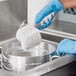 A person wearing blue gloves cleaning a pot with a white Lavex polyester scrub brush.