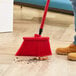 A person using a Lavex red broom to sweep a wood floor.