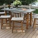 An Outdoor Interiors teak and composite counter height dining table with chairs and a plate of food on a deck.