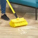 A person using a Lavex yellow bi-level scrub brush head to clean a wood floor.