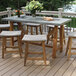 An Outdoor Interiors teak and ash wicker saddle stool on a table on a deck.