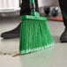 A person using a green Lavex broom to sweep a floor.