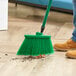 A person sweeping a wooden floor with a green Lavex angled broom.