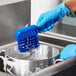 A person in blue gloves using a Lavex blue polyester utility brush to scrub a pot.