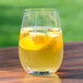 A Stolzle stemless wine glass with yellow liquid and fruit slices in it.