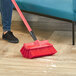 A person using a red Lavex bi-level scrub brush to clean a hardwood floor.